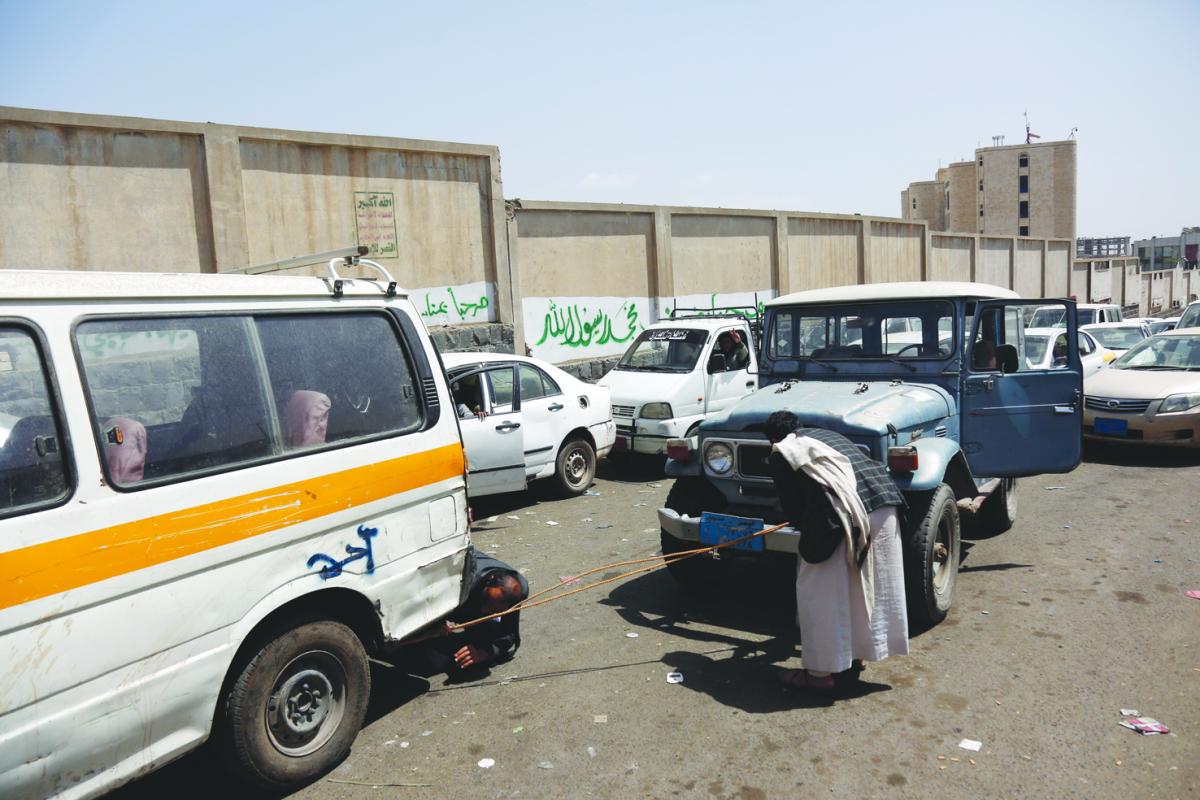رجلان يحاولان سحب سيارة انقطع وقودها أثناء الانتظار أمام إحدى محطات البنزين المكتظة في صنعاء (غيتي)